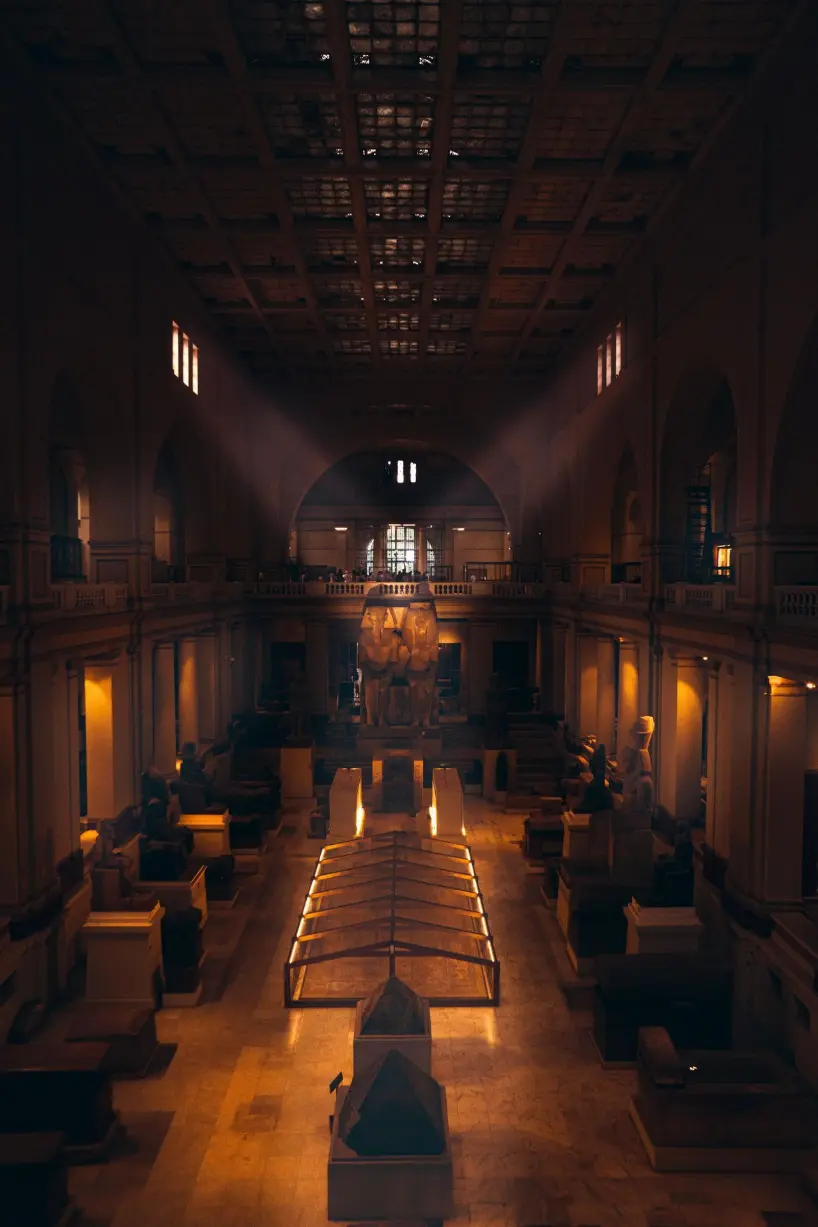 Interior of the Grand Egyptian Museum in Cairo showcasing ancient Egyptian statues and artifacts under dramatic lighting.